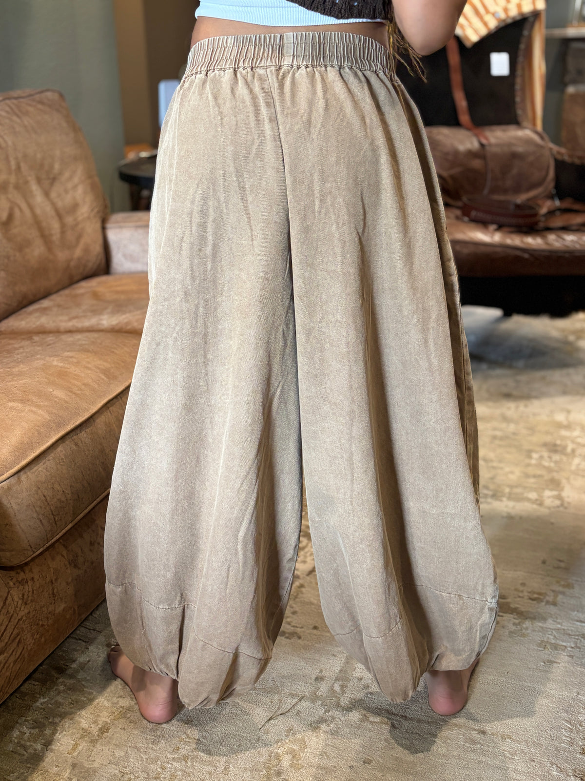 Back view of mocha pleated balloon pants showing the elastic waistband and rounded gathered legs.