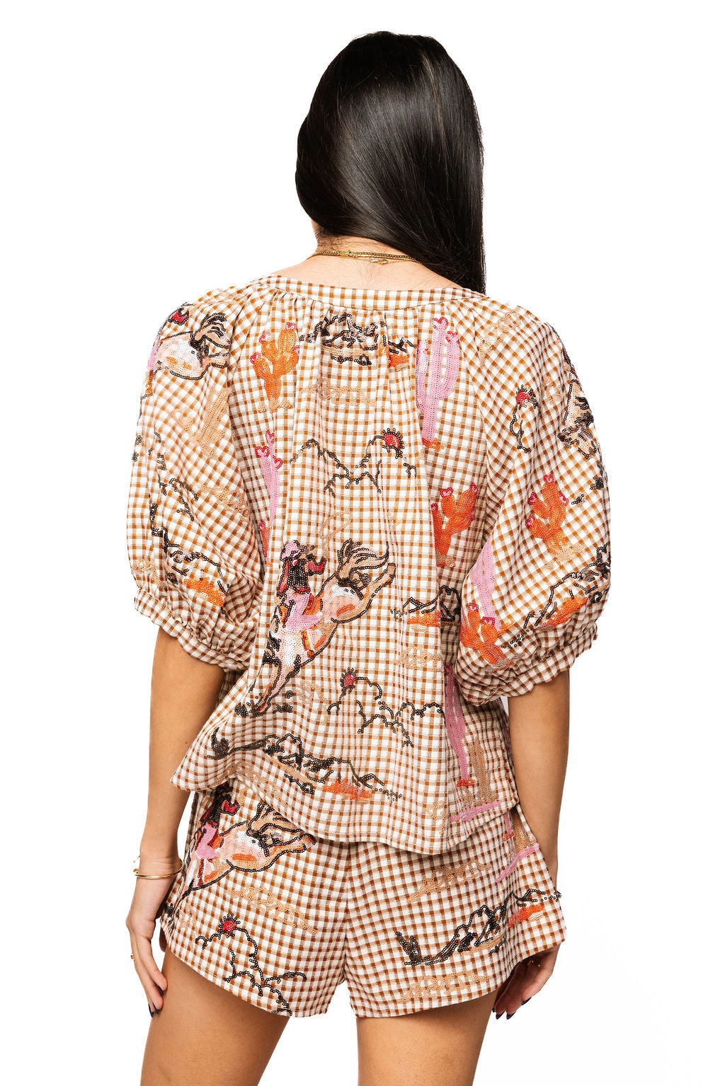 Back view of a model wearing the Queen of Sparkles brown gingham cowgirl top with colorful Western motifs and three-quarter sleeves.