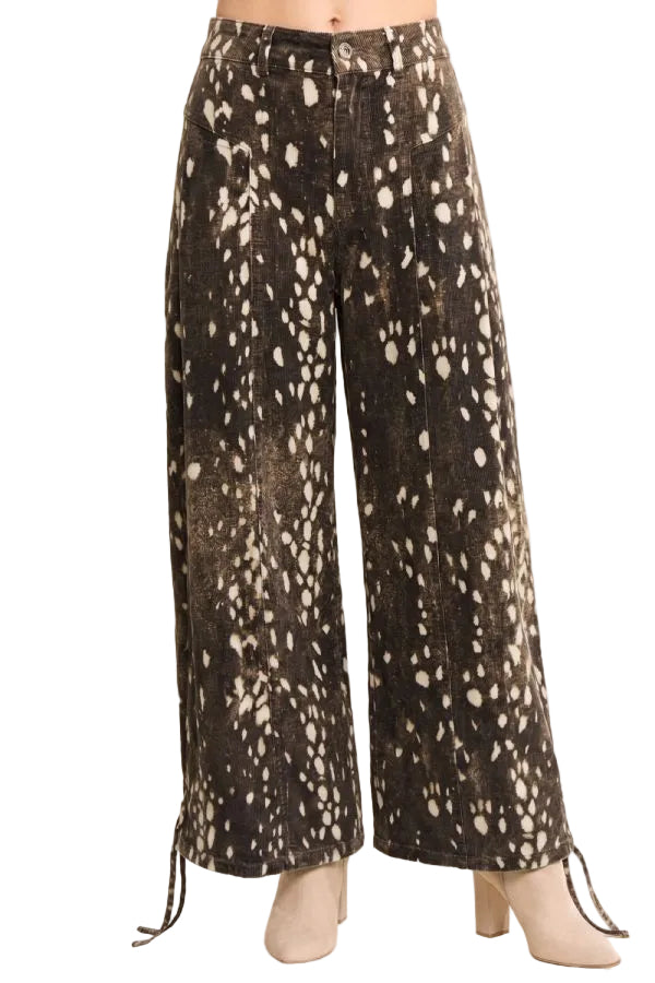 Front view of a model wearing chocolate brown fawn print wide leg pants with cream spots, front pockets, and belt loops.