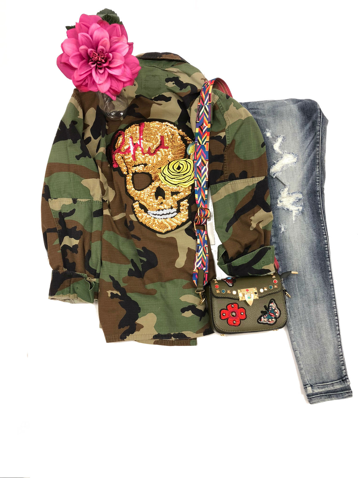 Flat-lay styling of the camouflage jacket with its gold sequin skull and rose back design, beside jeans and accessories