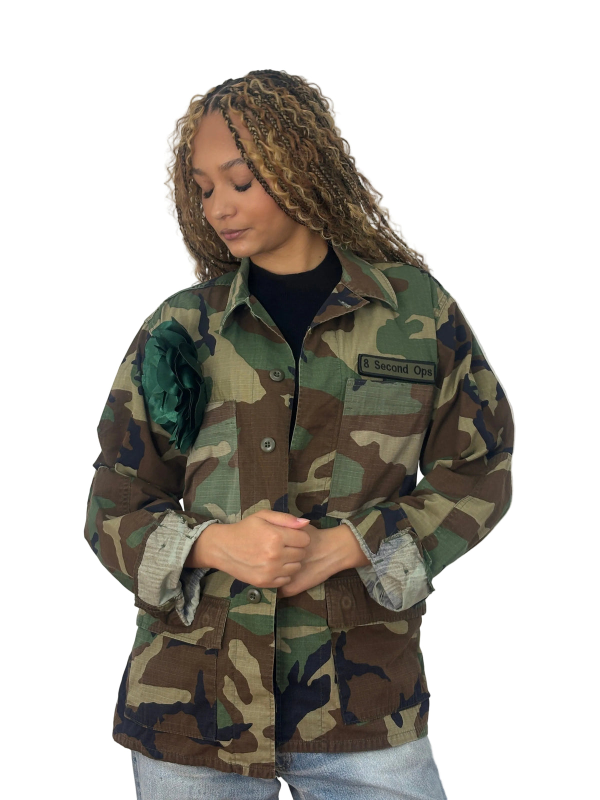 Front view of vintage camouflage field jacket with a dark-green fabric flower on the chest, buttons, and flap pockets