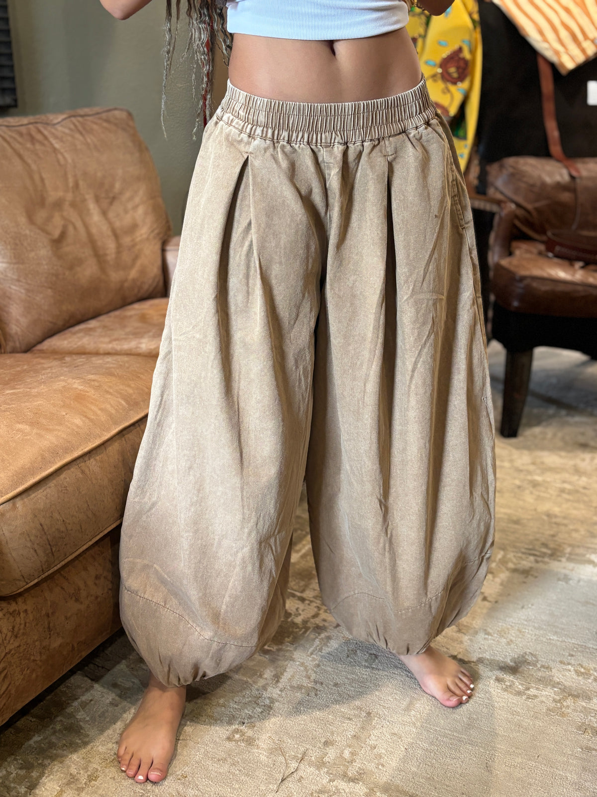 Front lifestyle view of mocha pleated balloon pants with a wide balloon shape and elastic waistband.