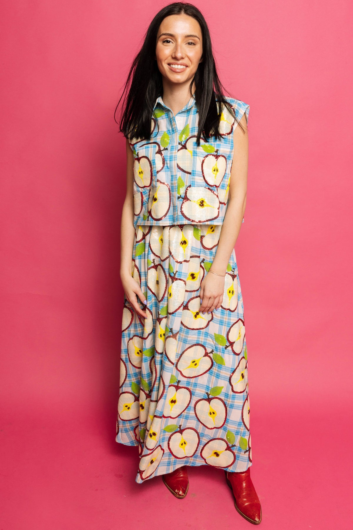 Smiling model in the Queen of Sparkles blue plaid apple-slice sleeveless tank and matching maxi skirt, shown full-length against a pink studio backdrop.