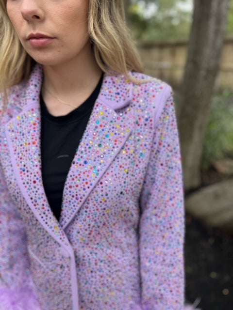Close-up of the lavender rhinestone blazer's notched lapel and colorful embellishments, with a feather cuff visible.