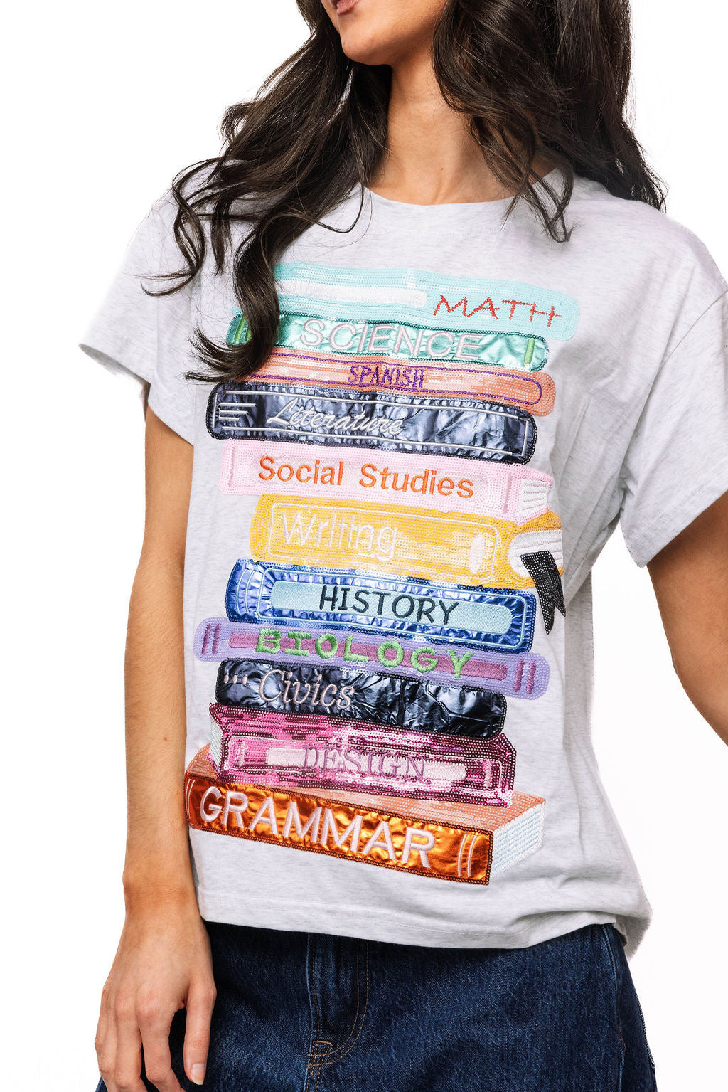 Front view of a model wearing the Queen of Sparkles beige School Books tee, with colorful stacked book graphics across the chest.