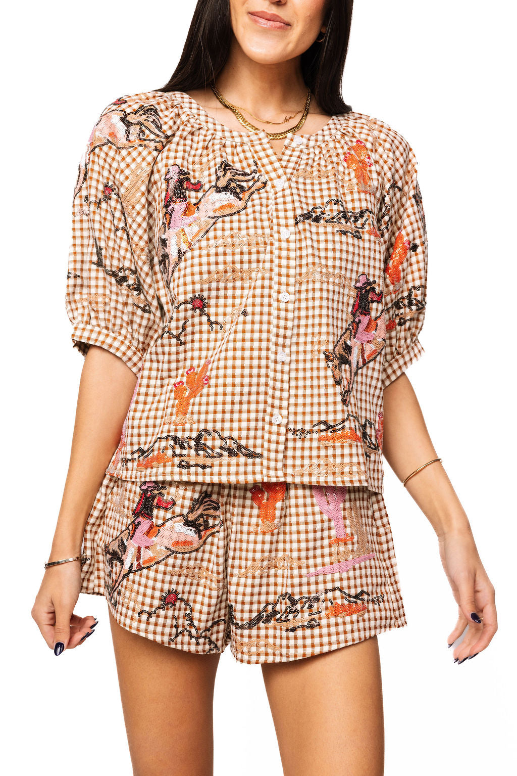 Front view of a model wearing the Queen of Sparkles brown gingham button-up top with colorful cowgirl and Western motifs; matching shorts are also shown.