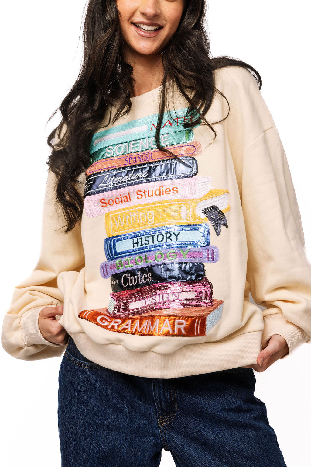 Front view of beige Queen of Sparkles sweatshirt with colorful stacked school-book design