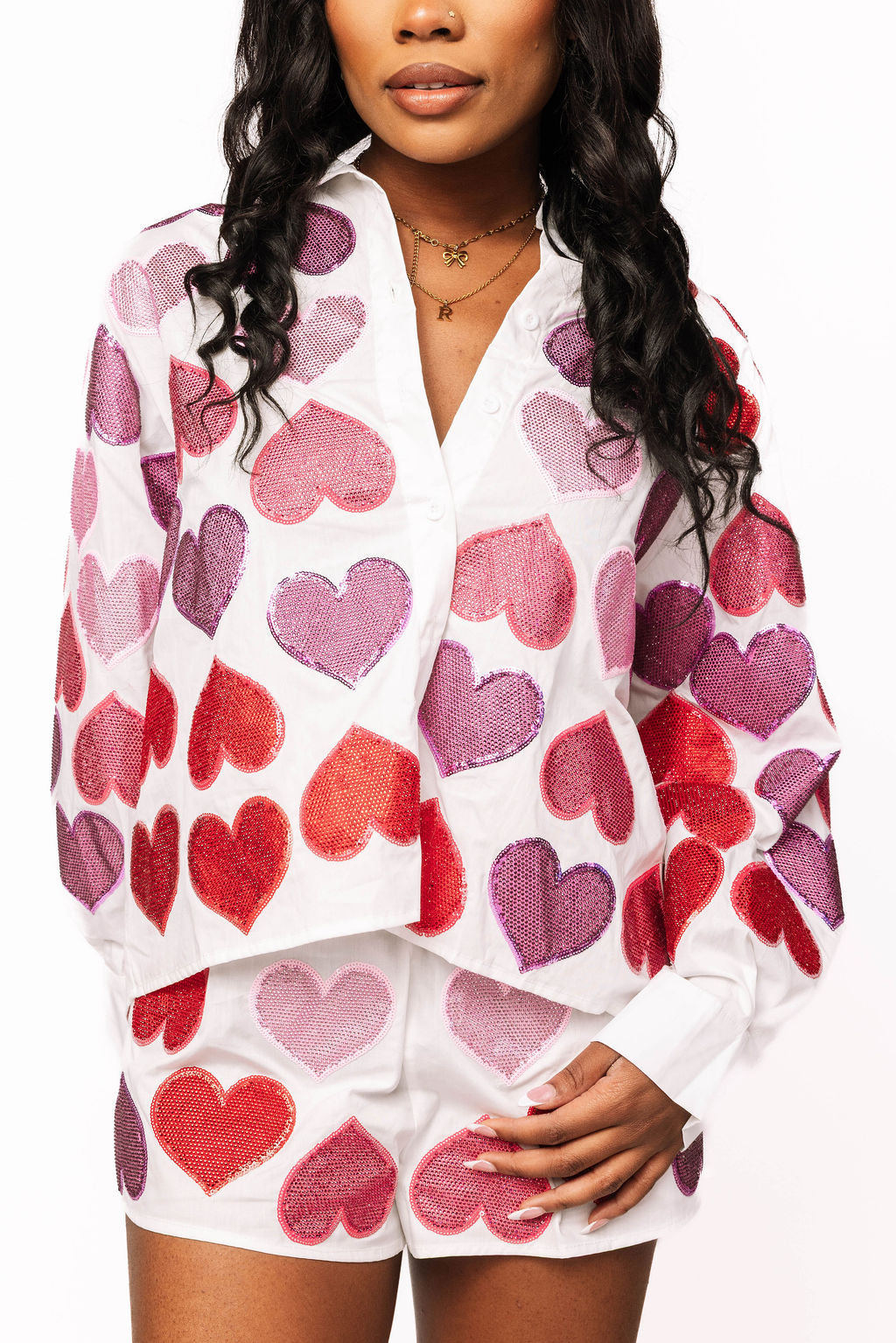 Front view of a white button-up cotton top covered with sparkling red, pink, and purple heart shapes.