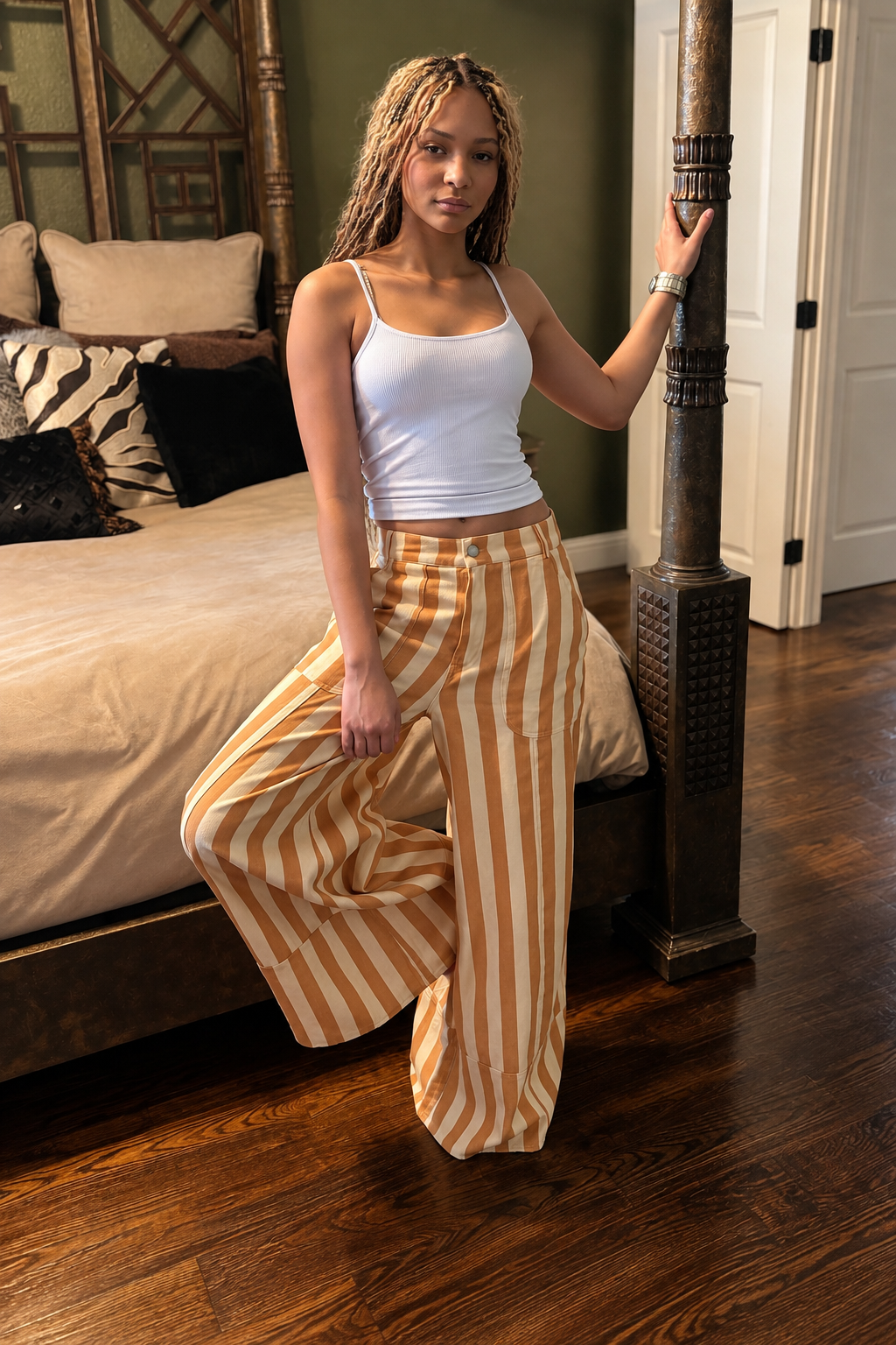 Side view of model wearing mustard and cream striped wide-leg pants with a white tank indoors.