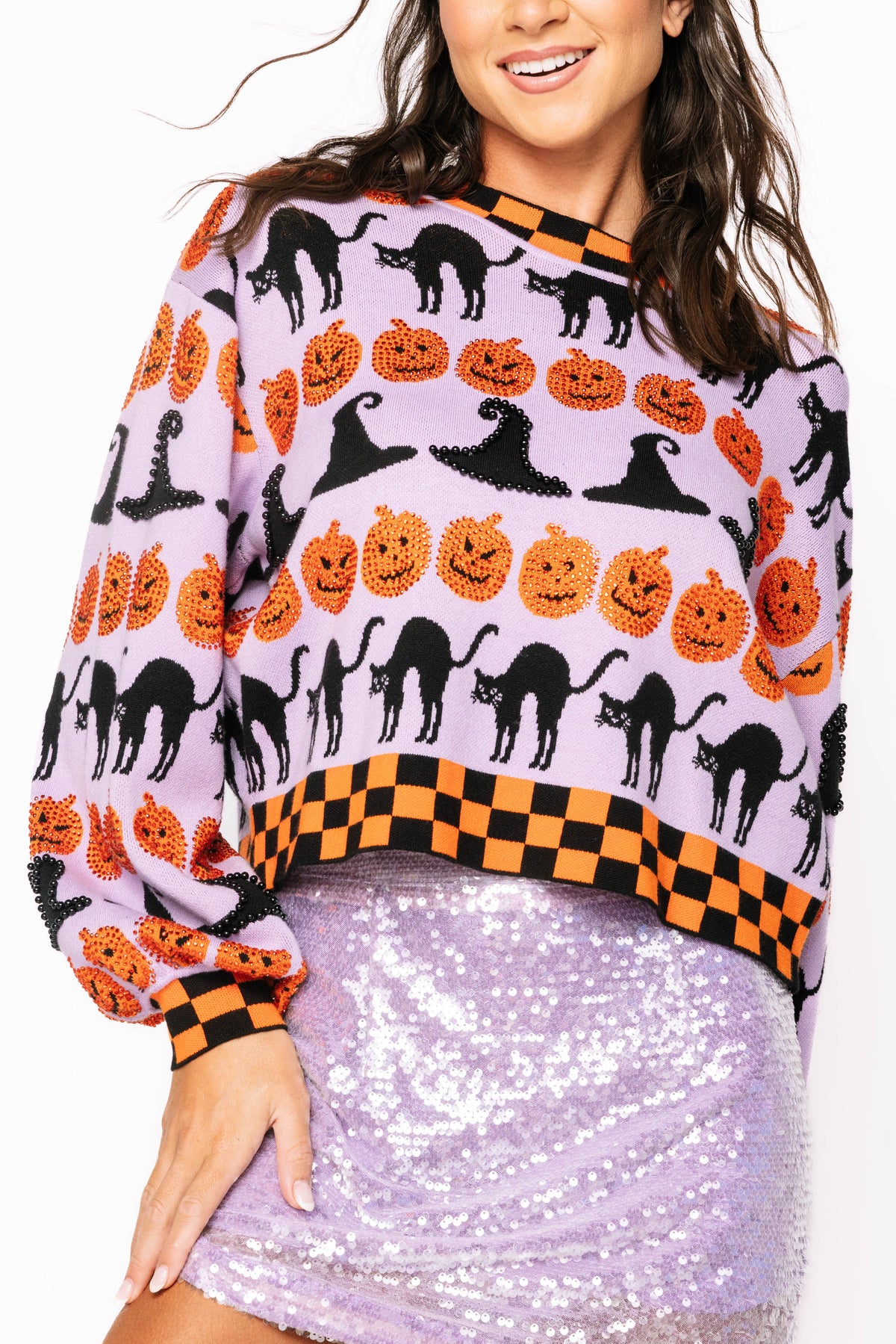 Front detail of a model wearing the Queen of Sparkles lavender Halloween sweater, showing black cats and witch hats, orange pumpkins, and black-and-orange checker trim.