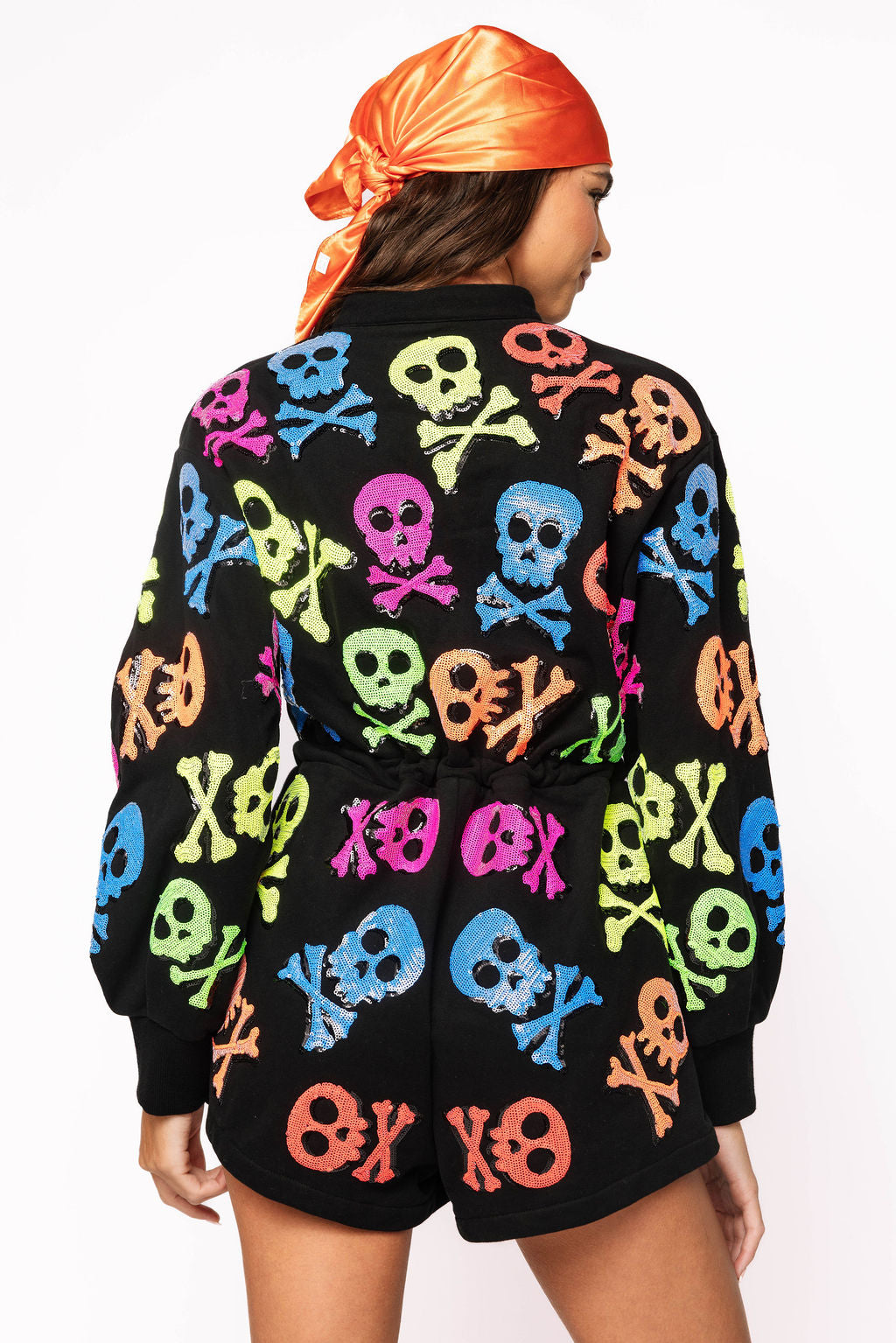 Back view of the Queen of Sparkles black long-sleeve romper, showing neon pink, blue, green, and orange skull-and-crossbones motifs across the back and sleeves.