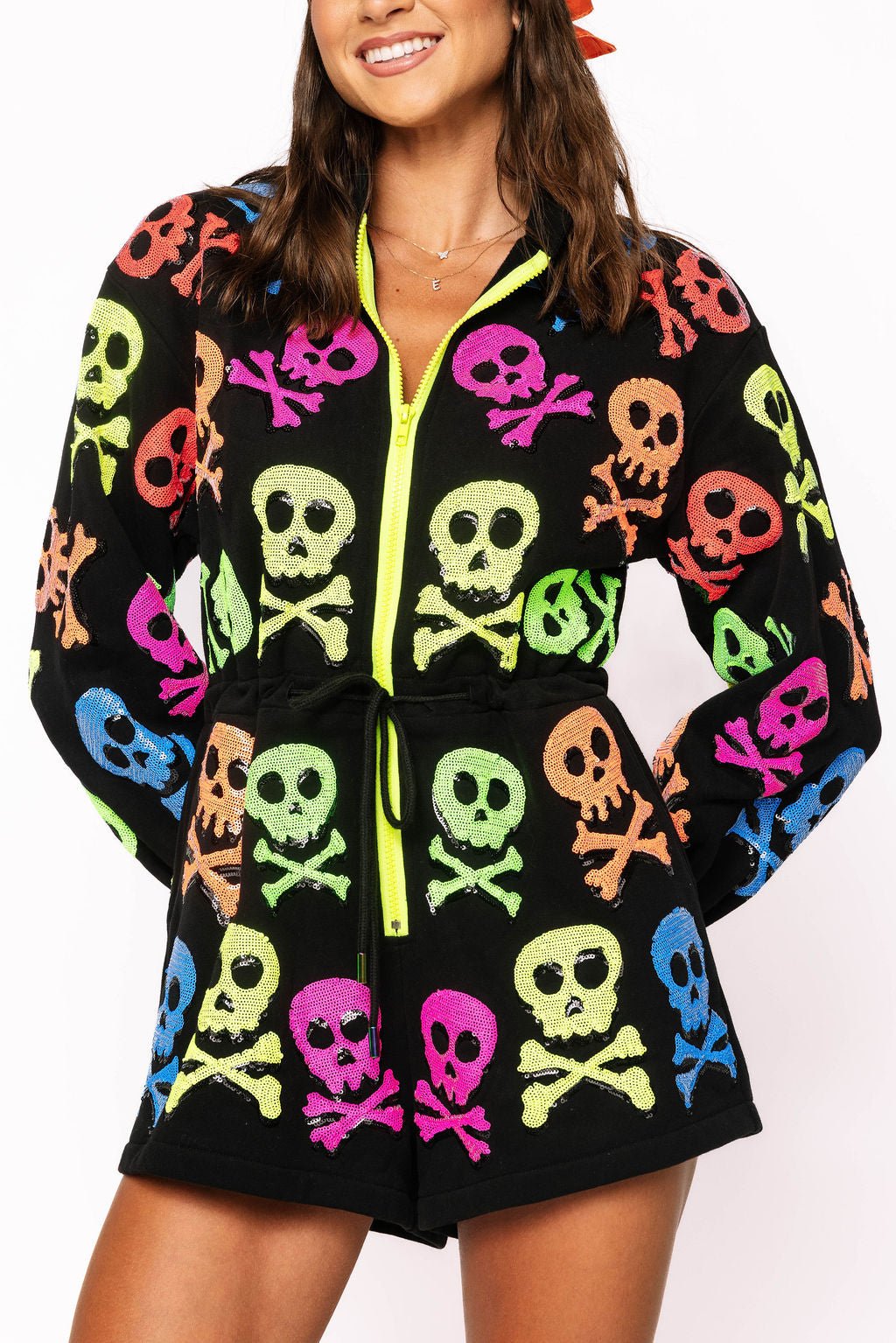 Model wearing the Queen of Sparkles black long-sleeve romper, front view showing colorful neon skull-and-crossbones motifs and lime front zipper trim.