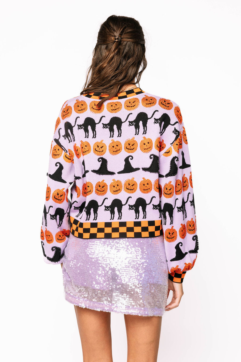 Back view of the Queen of Sparkles lavender sweater on a model, showing rows of black cats, pumpkins, witch hats, and checkerboard trim.