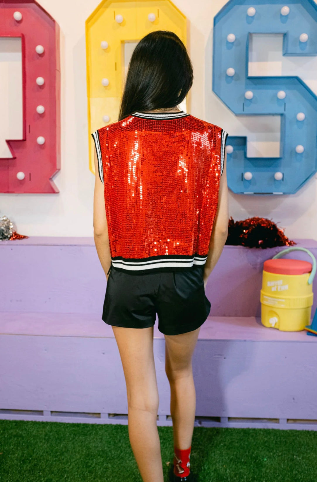 Back view of a model wearing a red sequin sweater tank with black-and-white striped trim, styled with a black skirt.