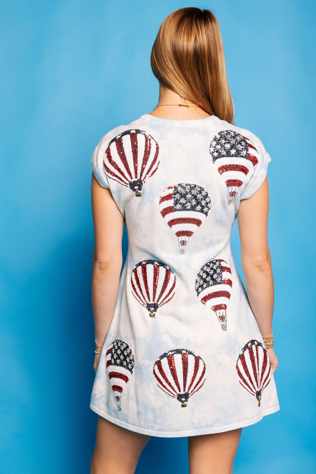 Back view of a model wearing the Queen of Sparkles light blue tie-dye Hot Air Balloon Sweater Dress against a blue background, showing the red, white, and blue balloon motifs.