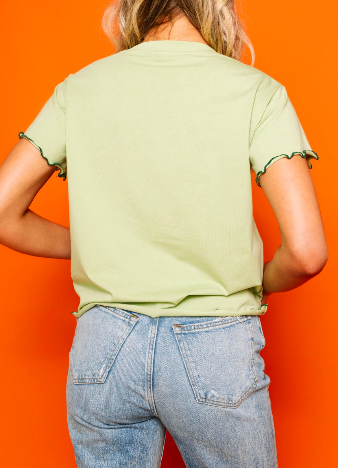 Back view of the light green shamrock top showing its frilly sleeve edges, against an orange background.