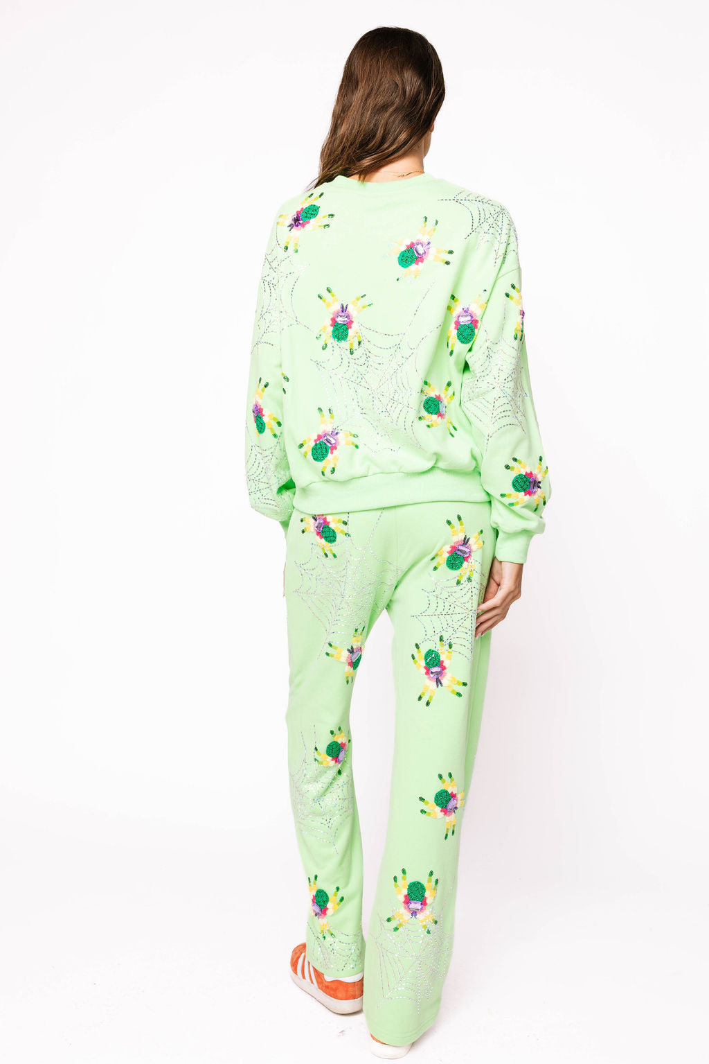 Full-length back view of a model wearing the neon light green Queen of Sparkles sweatshirt with colorful fuzzy spider motifs and rhinestone spiderwebs across the back and sleeves.