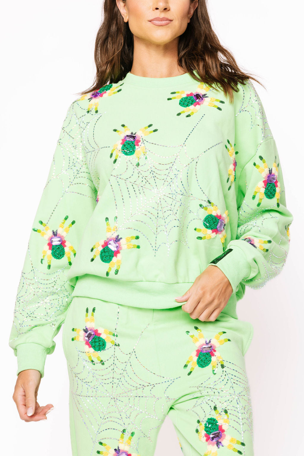Front view of a model wearing the neon light green Queen of Sparkles sweatshirt with colorful fuzzy spider motifs and rhinestone spiderwebs across the front and sleeves.