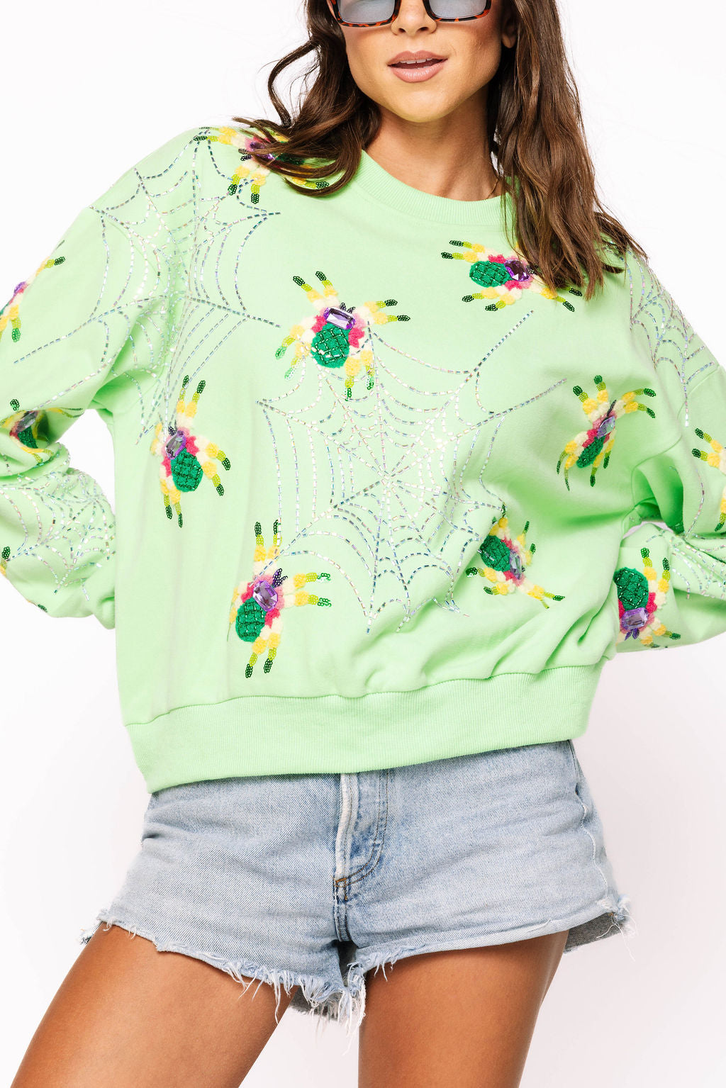 Front view of a model wearing the neon light green Queen of Sparkles sweatshirt with colorful fuzzy spiders and rhinestone web lines across the front and sleeves.
