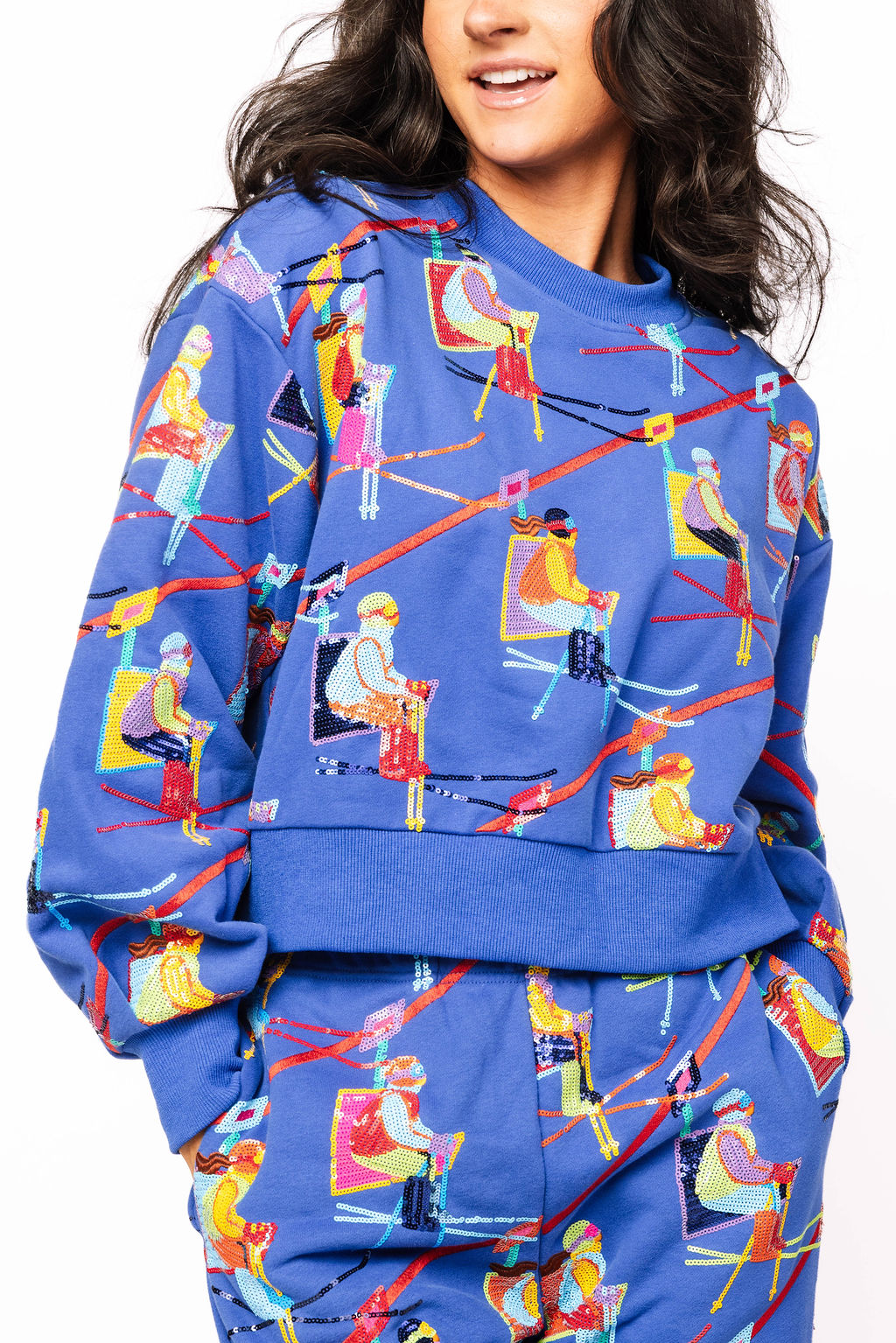 Model wearing the Queen of Sparkles royal blue sweatshirt with colorful skier and ski-lift motifs.