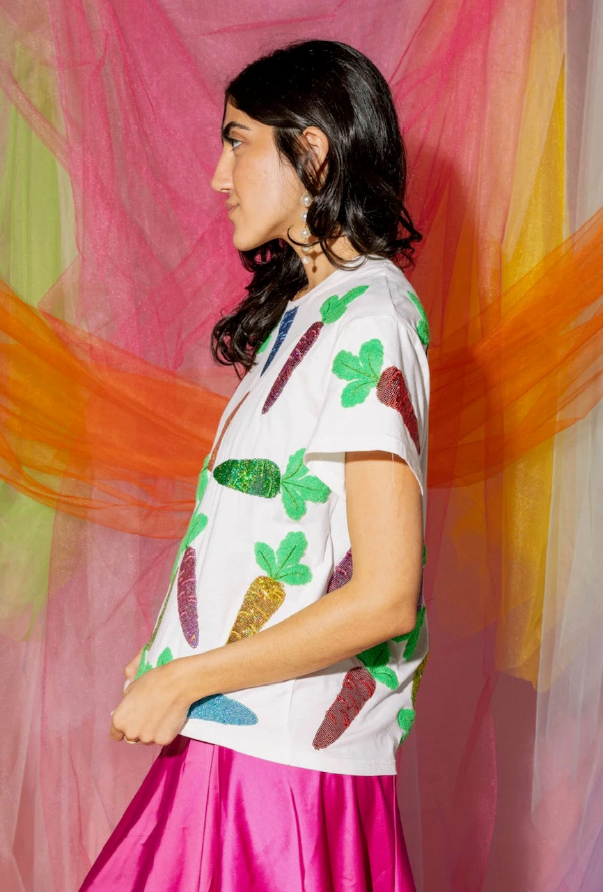 Side view of a model wearing the Queen of Sparkles white short-sleeve tee with colorful sequined carrot motifs, styled with a magenta skirt.