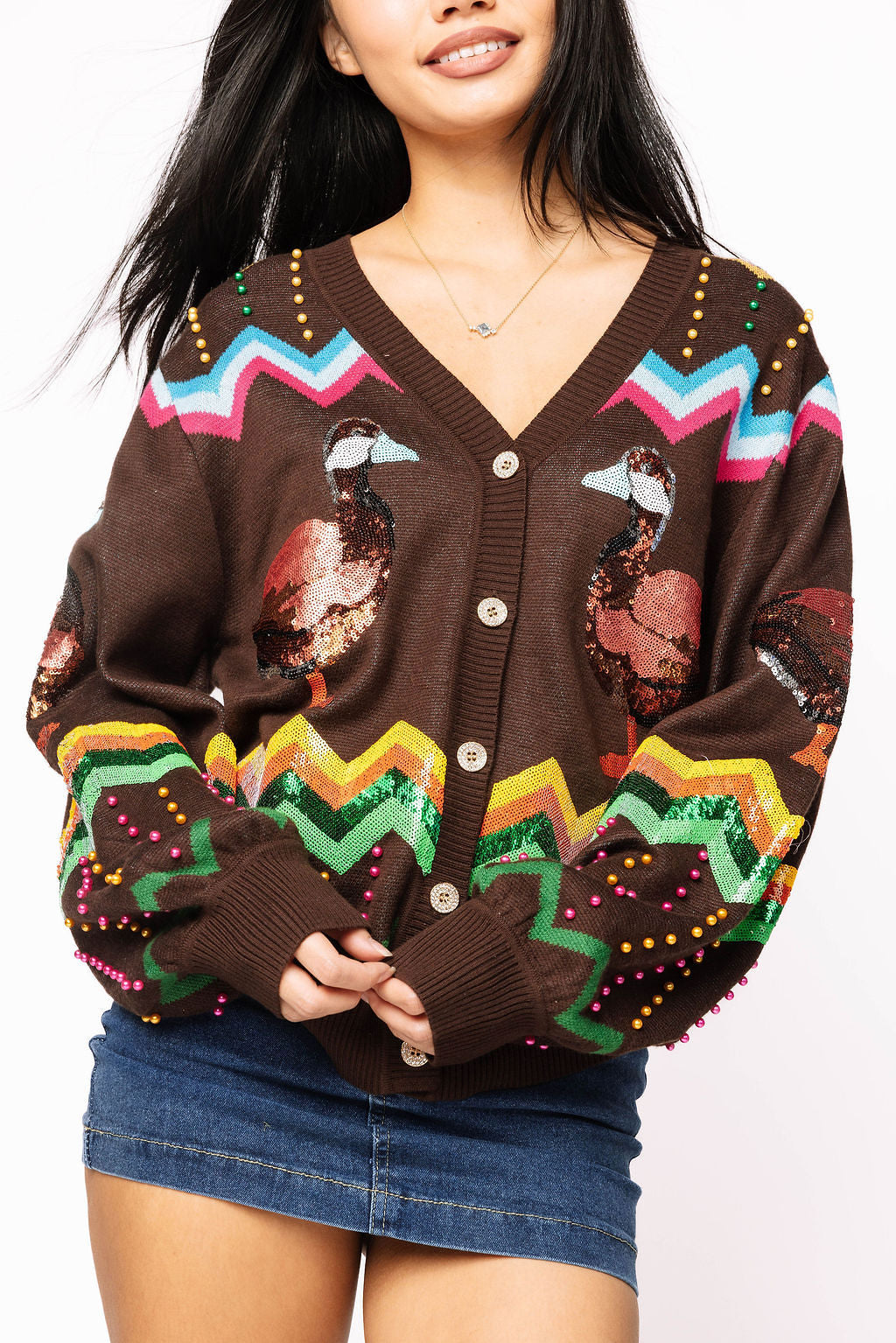 Front view of a model wearing the brown Queen of Sparkles duck cardigan with a V-neck button front, duck motifs, multicolored zigzag bands, and dotted embellishments.