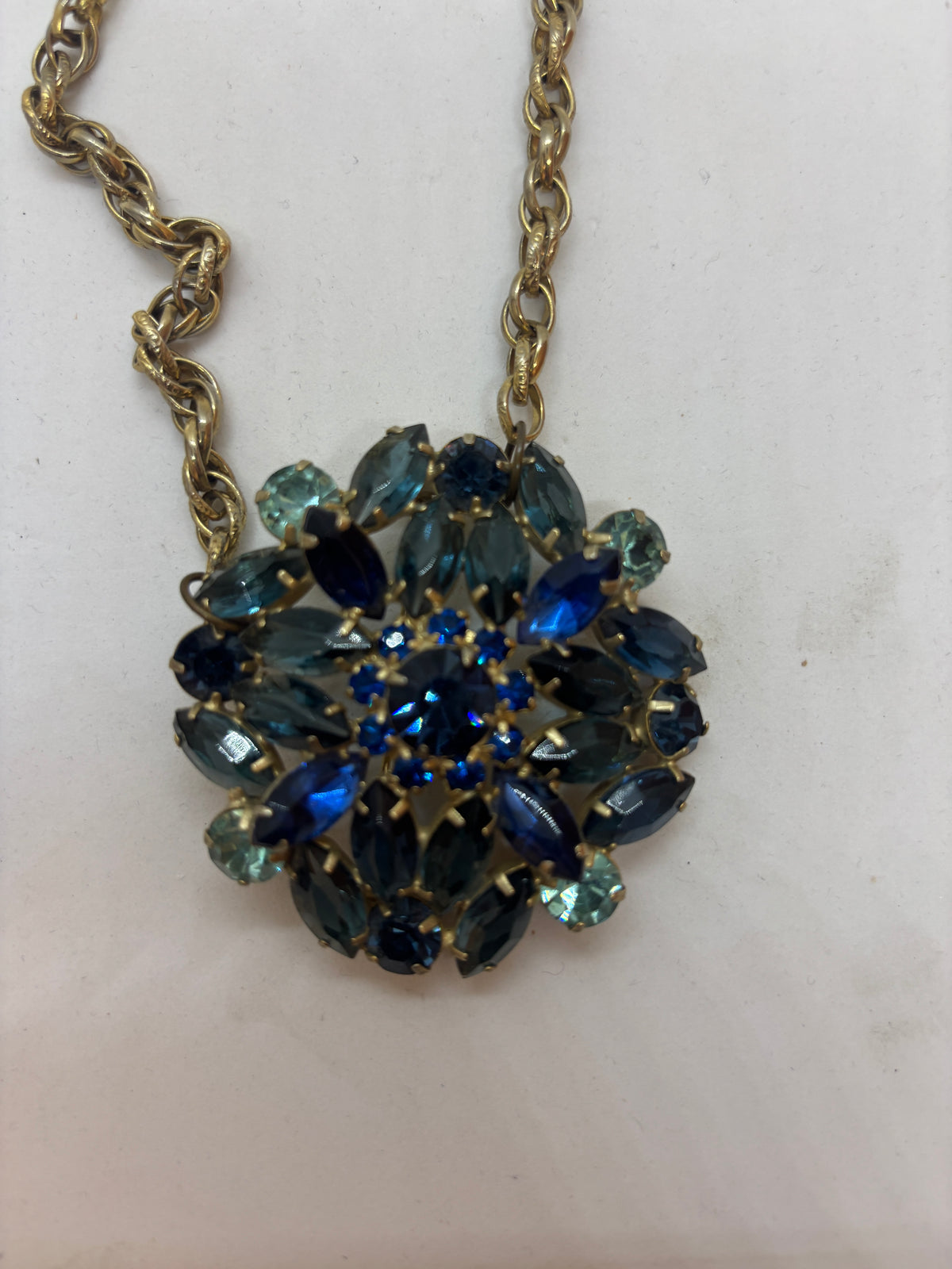 Close-up of vintage floral rhinestone brooch featuring deep blue, teal and aqua stones in a gold-tone setting.